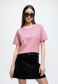 Ροζ ριγέ μπλουζάκι με λαιμόκοψη crew, συνδυασμένο με μαύρη φούστα από κοτλέ ύφασμα και μαύρη ζώνη. Το μοντέλο φοράει μεγάλα μαύρα γυαλιά ηλίου.