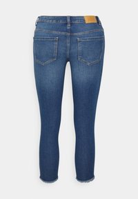 Skinny jeans azuis com um efeito desbotado, cintura média e bainhas desfiadas. Apresenta um patch de couro na parte de trás e dois bolsos traseiros.