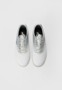 White athletic shoes with silver accents, a smooth synthetic upper, perforated details, and flat laces. Notable glitter effect near the toe.