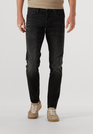 Zwarte denim jeans met een slim fit, voorzien van vijf zakken, contrasterende stiksels en een licht vervaagde textuur. Gecombineerd met beige sneakers.