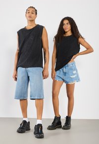 Črne brezrokavnike, svetlo modre jeans kratke hlače z raztrganimi robovi in črne čipkaste škornje. Preprost dizajn z udobnim krojem in teksturirano tkanino.