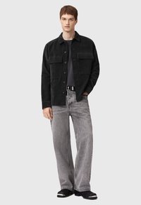 Black corduroy jacket with two chest pockets, paired with gray wide-leg jeans. Simple black shoes complete the outfit.