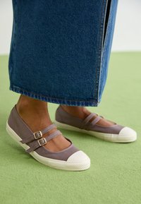 Zapatos planos de lona gris con puntera de goma blanca y dos correas ajustables. Presentan una parte superior textil y una suela texturizada.
