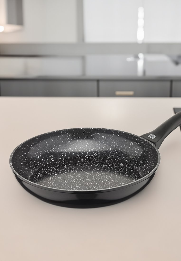 Nepřilnavá pánev s černým vnitřkem zdobeným bílými skvrnami, zaoblenými okraji a ergonomickou černou rukojetí. Plochý základ.