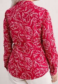 Camisa roja con estampado floral blanco, de manga larga y collar de botón. Confeccionada en una tela texturizada con un corte relajado.