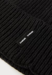 Black ribbed knit beanie featuring a woven label with "SAMISØE" text. Material appears soft; texture is thick and warm.
