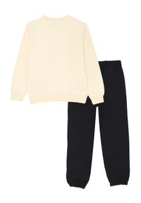 Felpa a maniche lunghe color crema abbinata a pantaloni jogger neri con vita ed estremità elastiche, stesi su uno sfondo bianco.