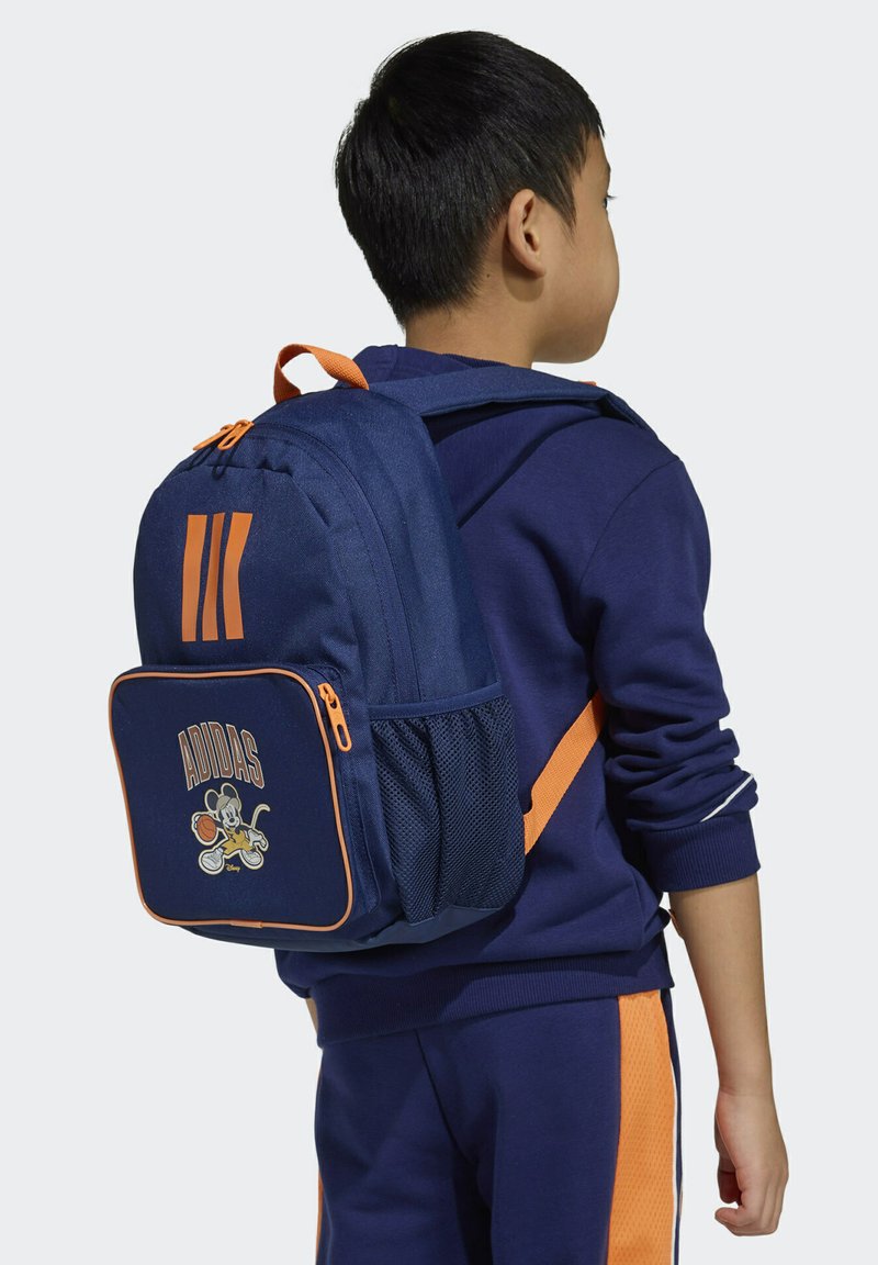 Tamnoplavi ruksak s narančastim detaljima, s više pretinaca na zatvarač i bočnim mrežastim džepom. Adidas logotip s crtanom grafikom.