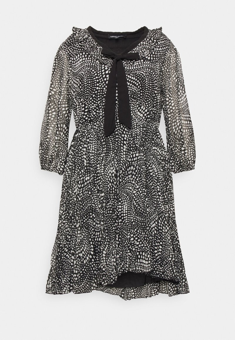 Robe noire longueur genou avec motif de points blancs irréguliers, manches bouffantes transparentes, col à volants et nœud noir à l'encolure.