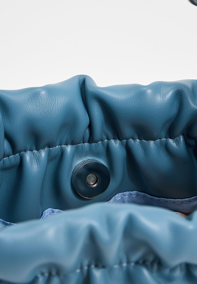 Pochette en cuir bleu avec un bord froncé, dotée d'une fermeture à bouton-pression en argent. La texture lisse et l'éclat subtil renforcent l'attrait visuel.