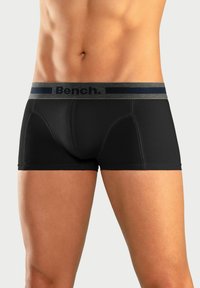 Black boxer shorts made of smooth fabric, featuring a gray waistband with navy text "Bench." and a fitted design that contours to the body.