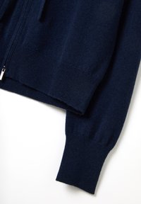 Marineblaue Strickjacke aus weicher, strukturiertem Wollmaterial, mit vollem Reißverschluss, gerippten Bündchen und einem offenen Ausschnitt.