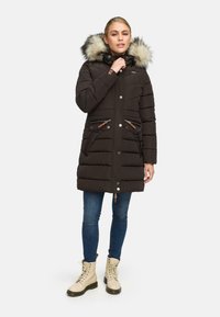 Svart vadderad parka med en huva som har pälsdetaljer, framfickor med tryckknappar och dragkedja, med bruna läderaccenter och en medellång design.