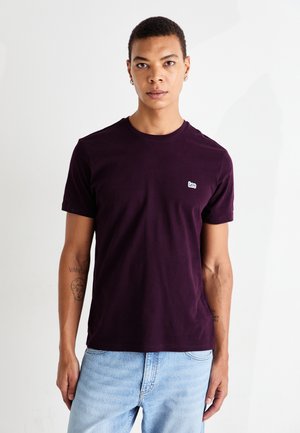 T-shirt di cotone viola con scollo rotondo e maniche corte, caratterizzata da un piccolo logo bianco "Lee" sul petto. Indossato con jeans azzurri chiari.