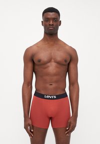 Röda kalsonger med svart midjeband som visar Levi's-logotypen, åtsittande design, tillverkade av slät tyg och midilång längd.