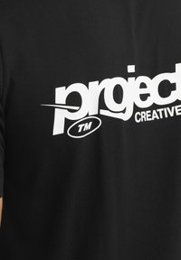 Camiseta de algodón negra con un destacado logo blanco que contiene el texto "project TM" y "CREATIVE" en negrita, situado en la parte frontal.
