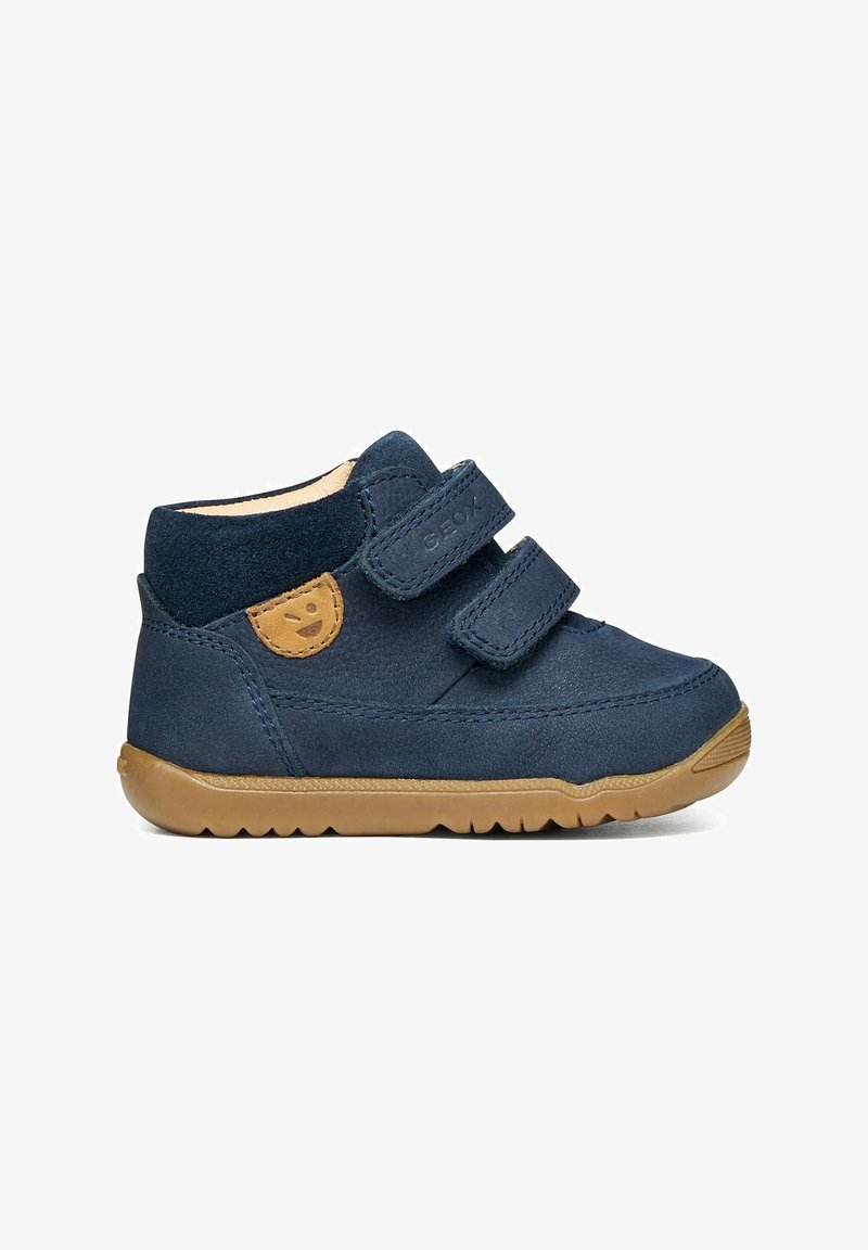 Chaussure pour tout-petit bleu marine avec deux bandes velcro, semelle en caoutchouc beige et patch beige avec visage souriant sur le côté.