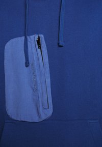 Felpa blu realizzata in tessuto morbido, con una tasca con zip di un blu più chiaro con logo, cordini e una tasca a marsupio frontale.