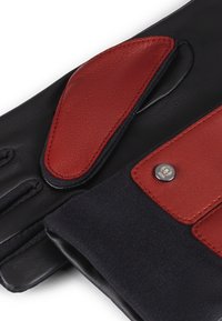 Guanti in pelle caratterizzati da un materiale nero scuro con accenti in pelle rossa. Presentano uno strato in tessuto morbido e un dettaglio in metallo con il logo.