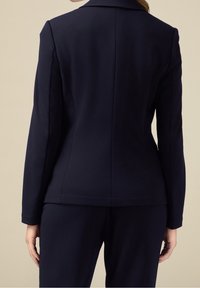 Blazer bleu marine ajusté avec une coupe structurée, doté d'un col cranté, d'une texture de tissu lisse et de coutures nettes le long des coutures.