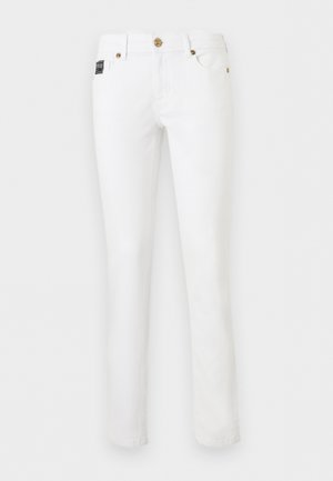 Jean blanc droit avec boutons et rivets dorés, poches avant et une petite étiquette de marque noire sur la poche droite.