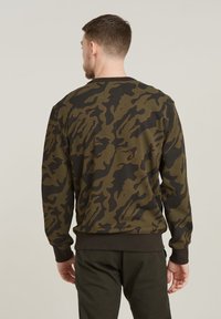 Sudadera de camuflaje en verde oscuro y negro con tejido texturizado, puños y dobladillo acanalados. Presenta un distintivo patrón abstracto.