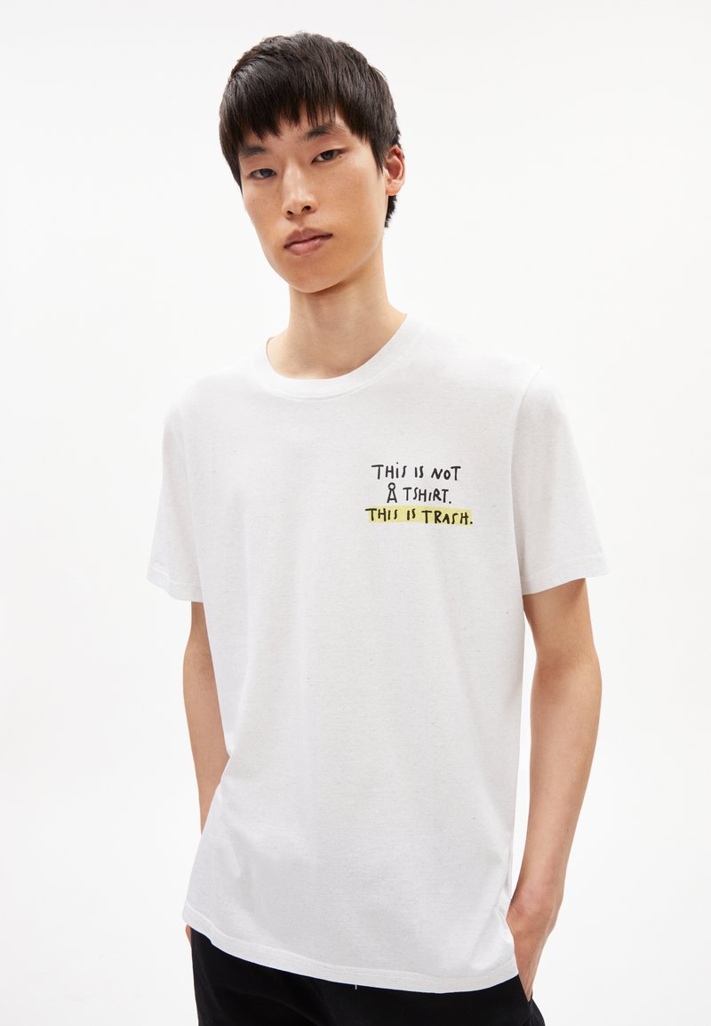 Witte katoenen t-shirt met zwart en gele tekst: "DIT IS GEEN T-SHIRT. DIT IS GEAFFIGEERD." Korte mouwen en ronde halslijn.