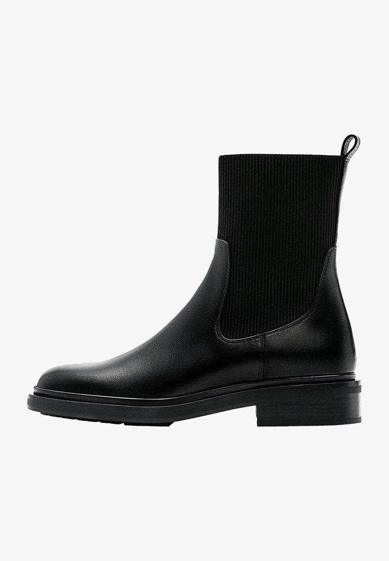Botte Chelsea noire présentant une base en cuir lisse et une tige en tissu côtelé, avec une languette de tirage et un talon bloc bas. Design classique pour un port polyvalent.