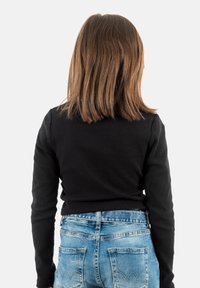 Un haut noir à manches longues côtelé associé à un jean en denim bleu clair ; le jean présente des détails de couture sur les poches arrière et une coupe décontractée.