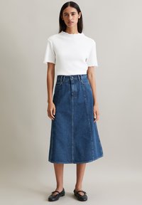 Haut blanc à côtes avec des manches courtes et des bords festonnés, associé à une jupe en denim bleu arrivant au genou avec des coutures frontales et des passants de ceinture.