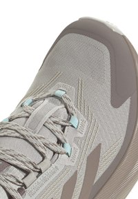 Grey athletic shoe with a mesh upper, turquoise accents, flat laces, and a textured sole. Features curved toe and reinforced heel.