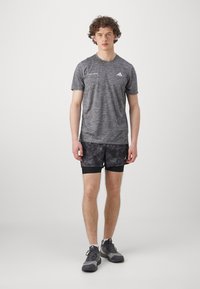 Grå atletisk T-skjorte med korte ermer, kombinert med svarte mønstrede shorts. Modellen har på seg grå sportsko med svarte detaljer.