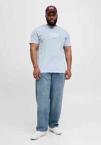 Lysblå t-shirt med korte ærmer med "Jack & Jones" logo, parret med løstsiddende blå jeans og hvide sneakers, toppet med en bordeaux kasket.