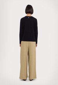 Maglietta nera a maniche lunghe con scollatura rotonda, abbinata a pantaloni beige larghi. Dettaglio notevole: piccolo accento sulla scollatura posteriore.