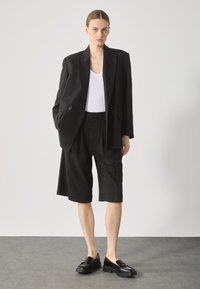 Svart oversized blazer med to knapper, kombinert med knelange svarte shorts og svarte loafers. Hvit tanktop under.