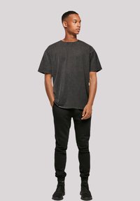 Black oversized T-shirt in a soft, faded fabric, paired with black tapered joggers and black sneakers, highlighting a relaxed fit and casual style.