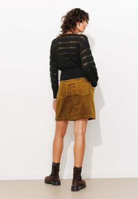 Pull en tricot à rayures noires avec une taille ajustée, associé à une jupe en velours côtelé de couleur moutarde comportant deux poches arrière et une coupe au genou.