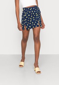 Marinblå tygkjol med tryck av gula citroner och körsbär, med sidoflikar, en figurnära design och en slät textur. Ihop med beige klackar.