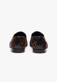 Zapatos de slip-on con estampado de leopardo que presentan un upper texturizado, detalles en cuero negro y una suela plana suave. Diseño elegante con patrones en contraste.
