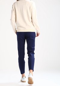 Beige texturerad tröja med rund hals som bärs med marinblåa smalare byxor; vita sneakers med en beige gummisula.