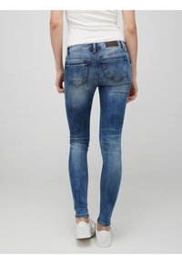 Smaljeans i blekt blå denim, med midje i normal höjd, en slät yta och två bakfickor. Bärs med vita sneakers.