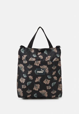 Sac fourre-tout Puma noir avec un motif floral beige et vert et deux poignées noires sur fond blanc.
