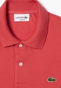 Rde polo majica Lacoste iz teksturiranega blaga, s tremi gumbi na ovratniku in zelenim izvezenim krokodilom na levi strani prsnega koša.