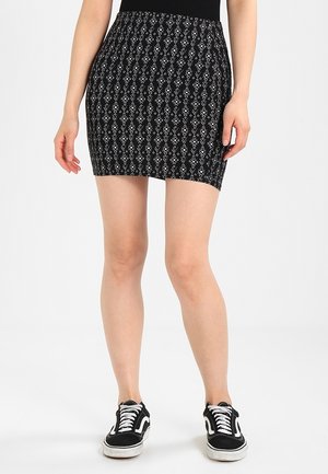 Jupe mini noire avec un motif géométrique blanc, taille élastique et coupe ajustée. Portée avec des sneakers noires.