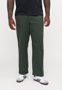 Pantalons droit vert foncé en tissu mélangé coton. Présente une texture lisse et des poches latérales, associés à des baskets blanches.