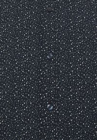 Camicia button-up blu navy con motivi geometrici bianchi sparsi, tra cui diamanti e stelle, con bottoni scuri e una trama liscia.