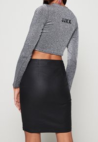 Kvinna i en silverglittrande kortärmad topp med texten "JJXX" på ryggen och en högmidjad svart penningkjol.