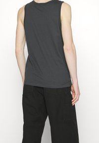 Grå ärmlös t-shirt gjord av bomull, med rak fåll och rund halsringning. Bärs med lediga svarta cargobyxor.