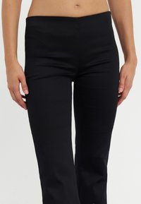 Czarne dopasowane spodnie wykonane z elastycznego materiału, charakteryzujące się gładką teksturą i wysokim stanem. Brak widocznych elementów metalowych lub wzorów.