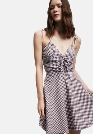 Ruudullinen mekko, jossa on tiukka yläosa, kerroksellinen yksityiskohta vyötäröllä ja säädettävät ohuet olkaimet. Väri kuviot sisältävät ruskeita ja valkoisia ruutuja.